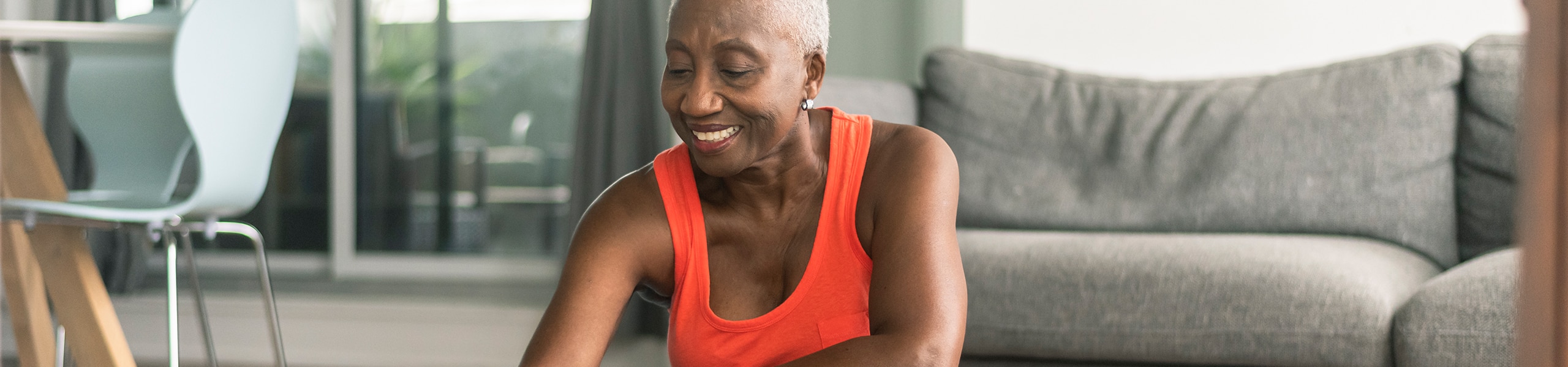 An older person smiles while sitting on a yoga mat